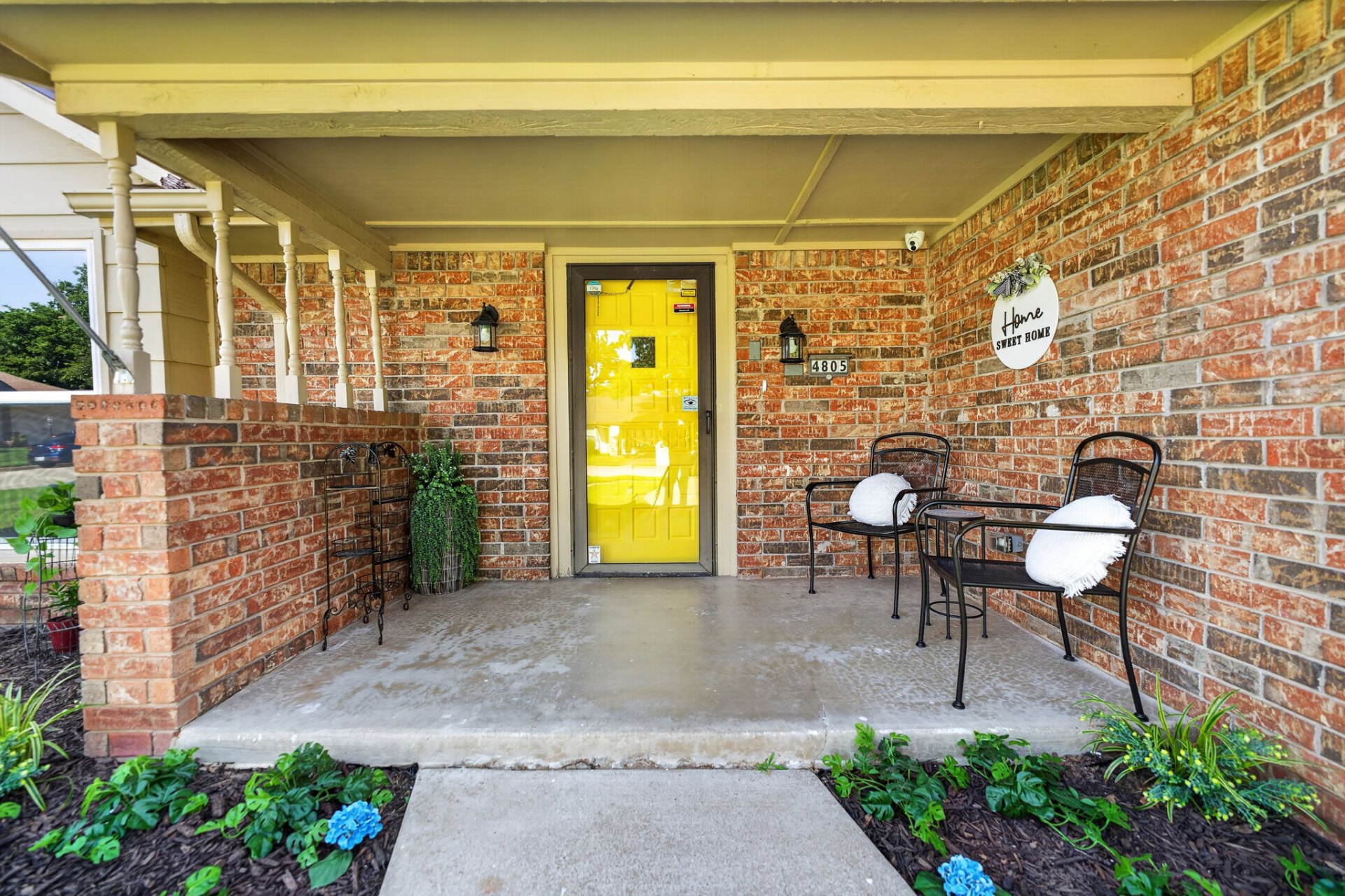 The welcoming front porch of Aspen with a bright yellow door and 'Home Sweet Home' sign